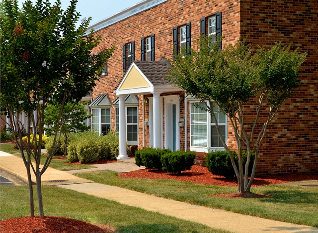 A brick building with a porch and trees in front.